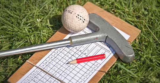 Ett golfprotokoll, en golfklubba, en golfboll och en blyertspenna ligger i gräset