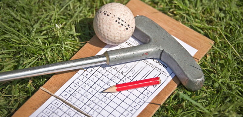 Ett golfprotokoll, en golfklubba, en golfboll och en blyertspenna ligger i gräset