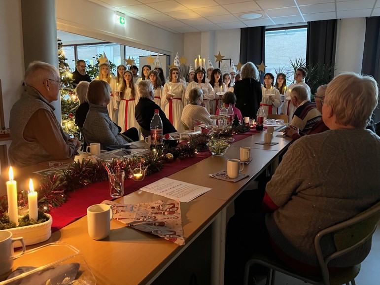 Lucia med tärnor och stjärngossar inför en publik vid fikabord
