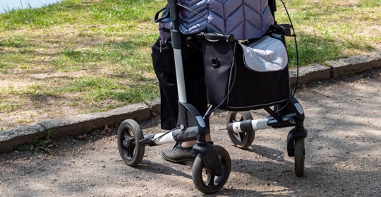 En dam i täckjacka sitter på sin rollator i på en parkgång