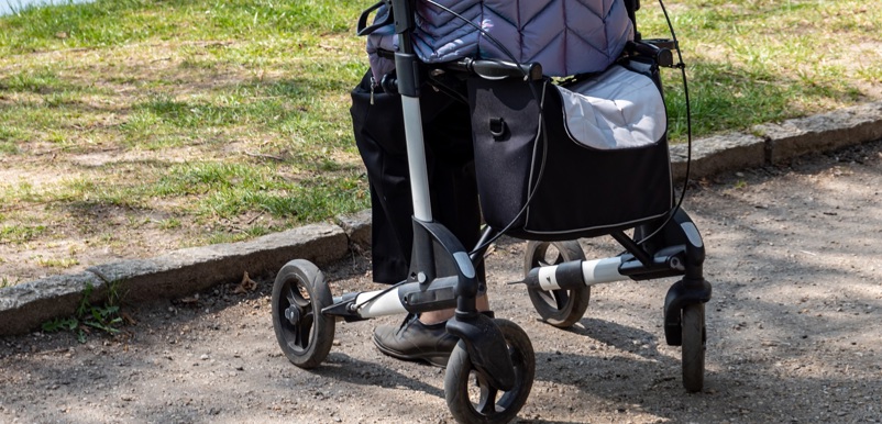 En dam i täckjacka sitter på sin rollator i på en parkgång