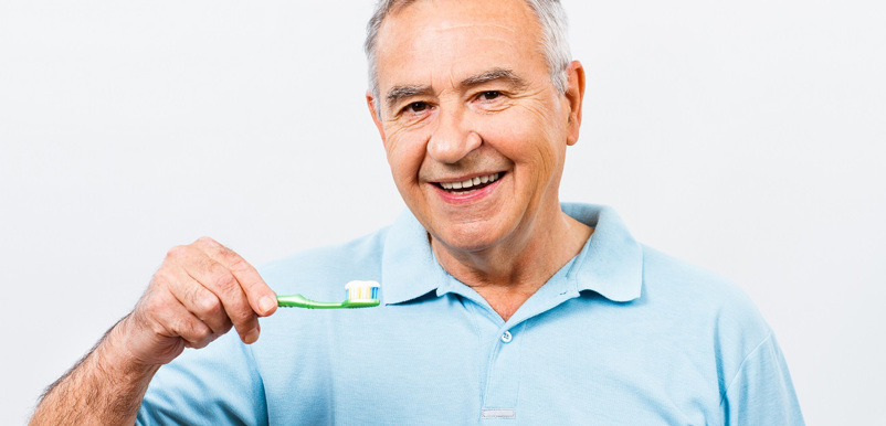 En glad äldre man håller upp sin tandborste