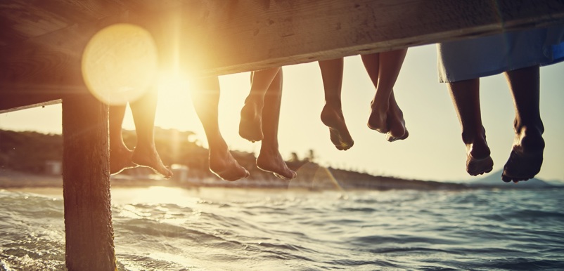 Fem personers fötter hänger ner från en brygga vid en sjö