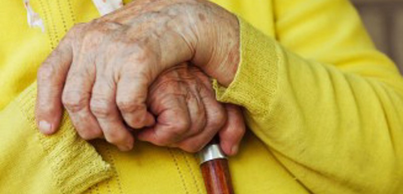 En person med gul kofta håller händerna på sin käppkrycka